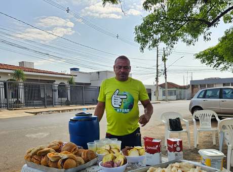 Voluntário do Atuar servindo café da manhã em mesa montada na rua